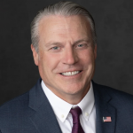Headshot of Brian Erickson in a business suit with USA flag pin