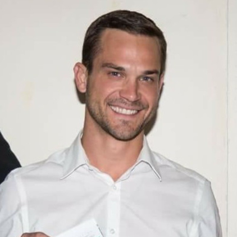 Dallin Young smiling in a white collared business shirt against a white wall