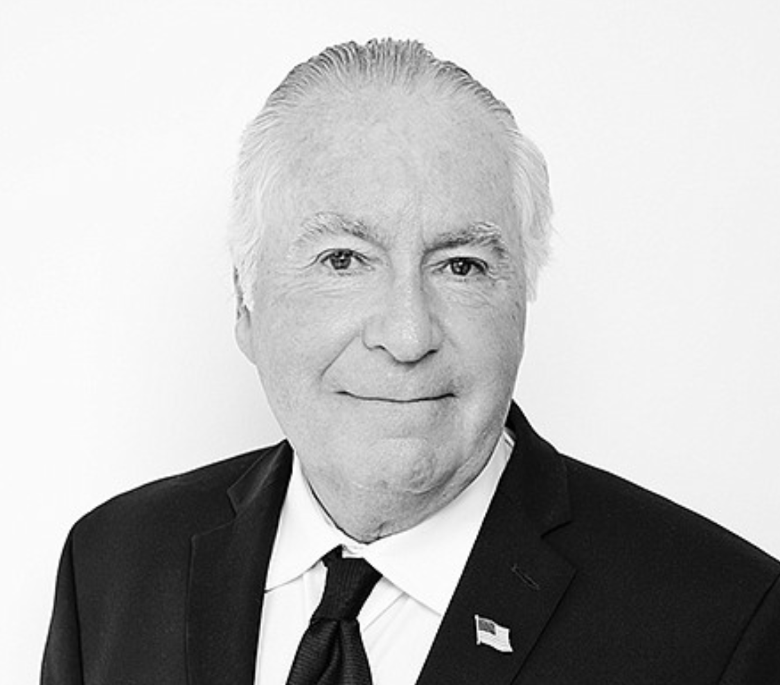 Black and white headshot of Dan Smiechowski in a dark business suit and tie with white collared shirt and a USA flag pin on white background
