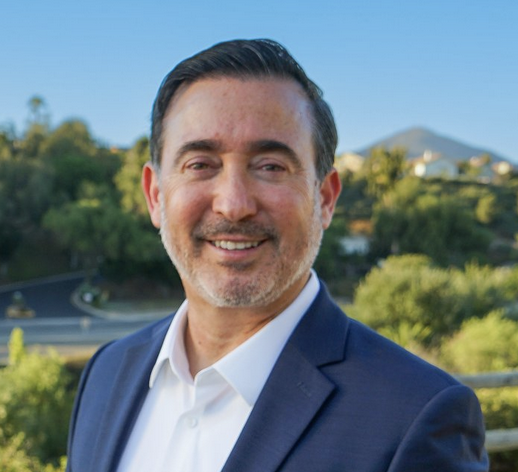 Headshot of Michael Inzunza smiling in a blue business suit and white collared shirt with a suburban street background with greenery