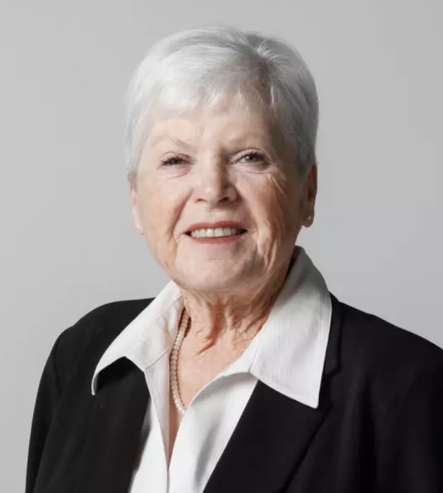 Picture of Nancy Casady smiling with black jacket and white collared shirt with white necklace against a light grey studio backdrop