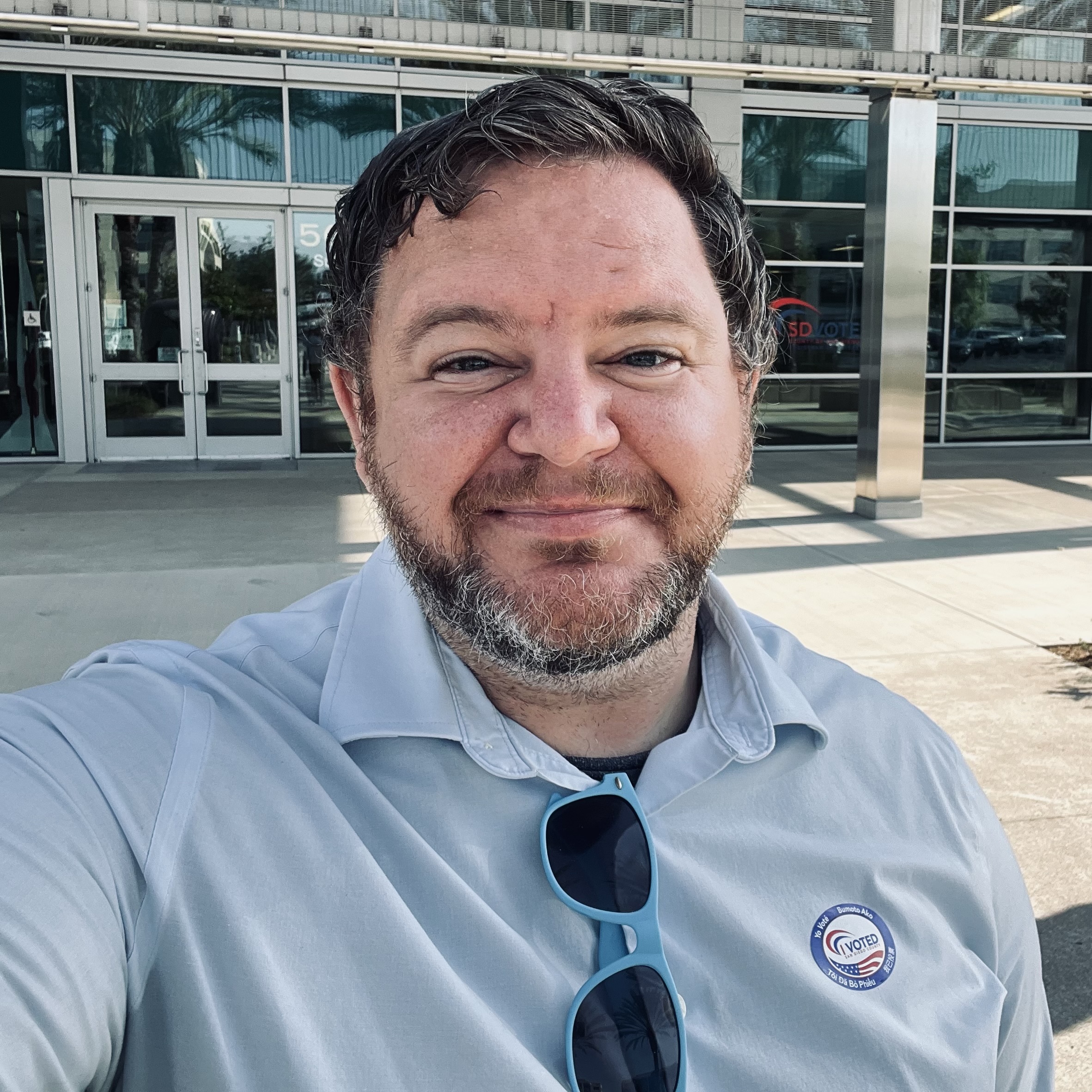 Picture of Ryan Trabuco smiling in a casual collared shirt in front of the county voter registrar building