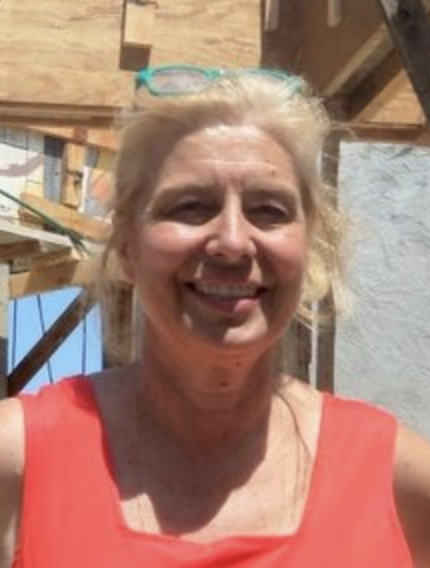 Picture of Christine Brady smiling on a bright sunny day in a reddish orange sleeveless top with construction in the background