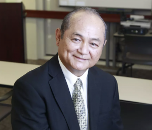 Godwin Higa smiling in a black business jacket with tie and white collared shirt