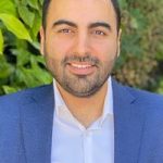 Jonathan Elist smiling in a blue business jacket and white collared shirt with greenery in the background