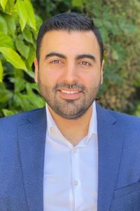 Jonathan Elist smiling in a blue business jacket and white collared shirt with greenery in the background