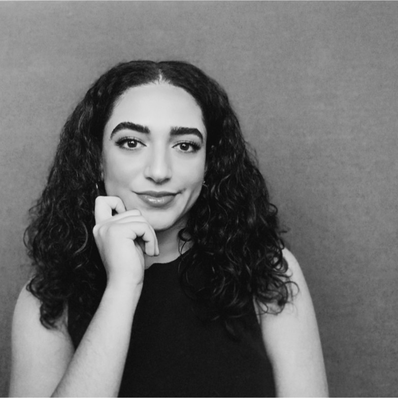 Black and white picture of Leila Khader smiling in dark top against grey background