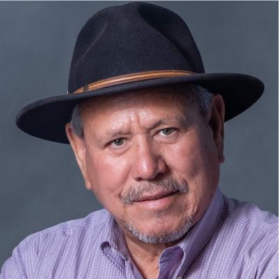 Headshot of Octavio Aguilar in a light purple collared formal shirt with black brimmed hat against a grey backdrop