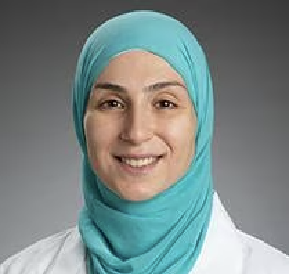 Picture of Sarah Elfeky smiling in a teal hijab and white physician's coat against a grey background