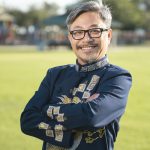 Picture of jean-huy tran in an ao dai wearing glasses on a bright sunny day in front of a blurred public park